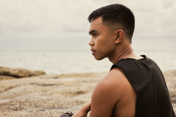 Naklejka na ściany i meble Serious profile portrait of Filipino man by the sea. Pensive male person alone with contemplation look outdoors. Inner peace concept