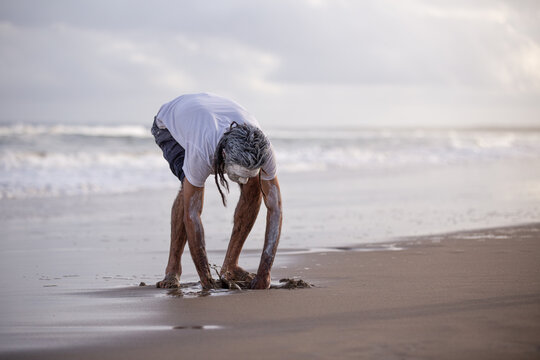 Aboriginal man digging with his hands on a beach
