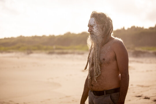Aboriginal middle aged man with clay face paint standing on a beach