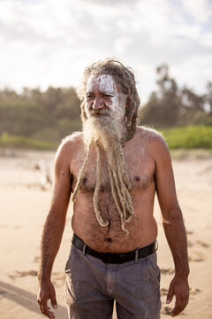 Aboriginal middle aged man with clay face paint standing on a beach