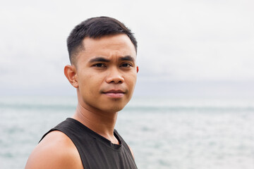 Serious portrait of young Filipino man by the sea on cloudy day. Asian male model concept