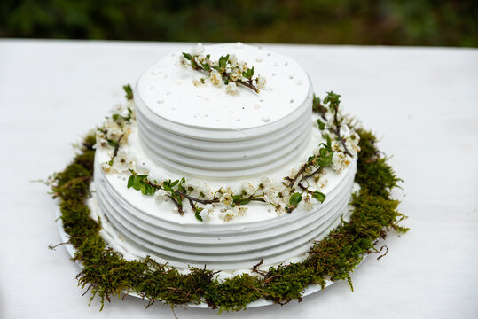 Wedding cake. Close-up photo of a beautiful white two-tiered wedding cake decorated by flowers and greenery
