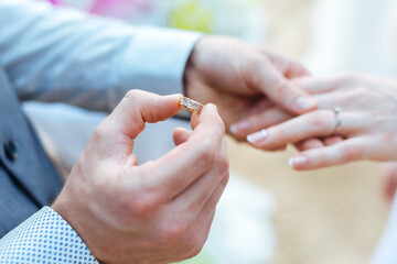Photograph of the groom holding the bride's hand and putting on the engagement ring for the bride at the wedding ceremony located on sandy beach.
