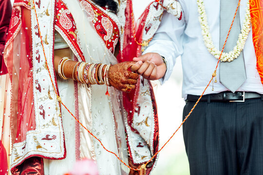 Indian wedding ceremony bride and groom holding hands together There are accessories such as rings, necklaces, bracelets, garlands and Henna tattoos on the hands of the bride. looks very magical.