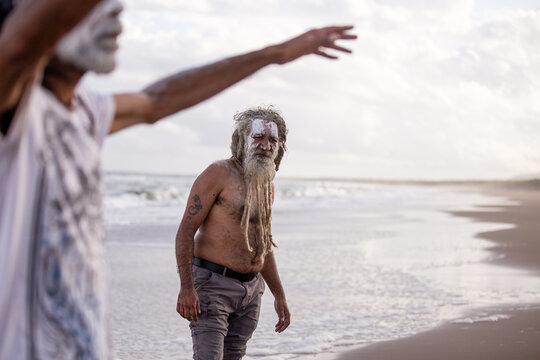 Aboriginal middle aged man listening to another Aboriginal man talking on a beach