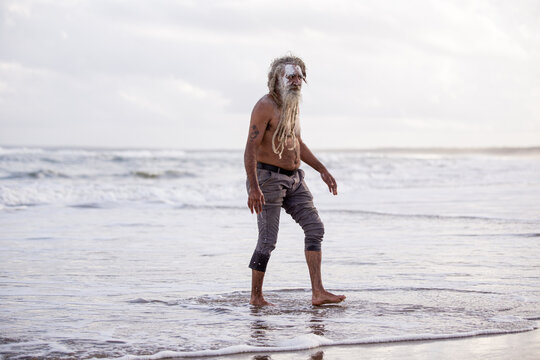 Aboriginal middle aged man walking through water on a beach looking at the camera
