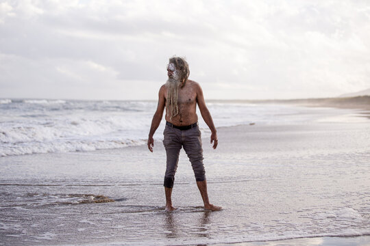 Aboriginal man standing in ankle-deep water on a beach