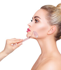 Fototapeta premium Young woman using pink quartz gua sha roller for face.