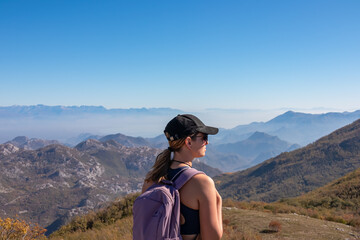 Naklejka premium Woman with backpack and hat on top of Goli Vrh with scenic view on mountain chains of Dinaric Alps and Lake Skadar National Park, Montenegro, Balkan, Europe. Valley covered by mystical fog. Freedom