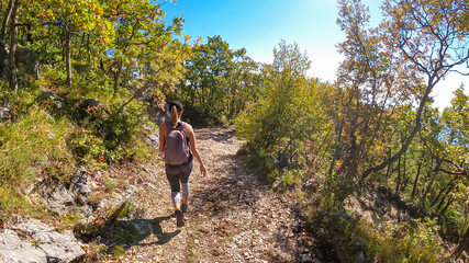 Obraz premium Woman with backpack on idyllic hiking trail through dramatic autumn forest from Sveti Stefan to Goli Vrh, Montenegro, Balkan, Europe. Sun beams shining through the plants creating magical atmosphere