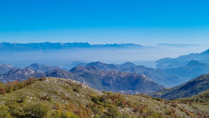 Panoramic view of dramatic karst mountain chains Dinaric Alps surrounding the Lake Skadar National Park seen from Goli Vrh, Montenegro, Balkan, Europe. Valley is covered by mystical fog, blue hills