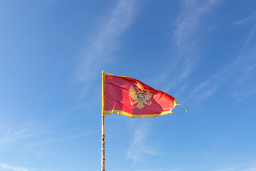 Montenegro flag blowing in the wind over nice blue sky background. Banner seen from St Ivan fortress in Kotor bay in sunny summer. Patriotism