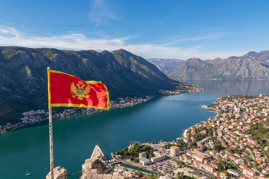 Montenegro flag blowing in wind with scenic view from St Ivan fortress on Kotor bay in sunny summer, Adriatic Mediterranean Sea, Montenegro, Balkan Peninsula, Europe. Fjord winding along coastal towns - Powered by Adobe