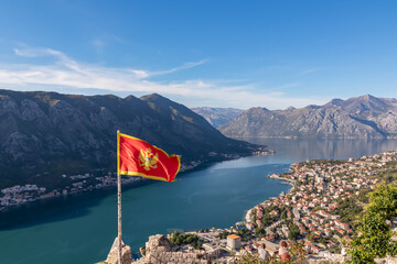 Montenegro flag blowing in wind with scenic view from St Ivan fortress on Kotor bay in sunny summer, Adriatic Mediterranean Sea, Montenegro, Balkan Peninsula, Europe. Fjord winding along coastal towns