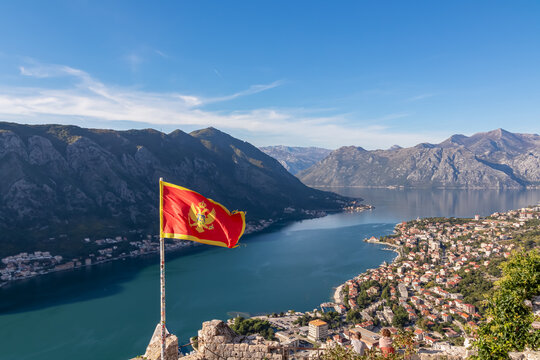 Montenegro flag blowing in wind with scenic view from St Ivan fortress on Kotor bay in sunny summer, Adriatic Mediterranean Sea, Montenegro, Balkan Peninsula, Europe. Fjord winding along coastal towns