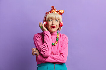 Senior Woman Listening Music. Positive Grandmother Listening Favourite Song Wearing Headphones and Enjoying. Indoor Studio Shot Isolated on Violet Background 
