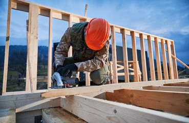Carpenter using circular saw for cutting wooden plank. Man worker building wooden frame house....