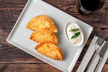 Beef Cheburek on a wooden table. Deep Fried Beef Dumplings with meat and onions. Turkish name Ci Borek or Cig Borek