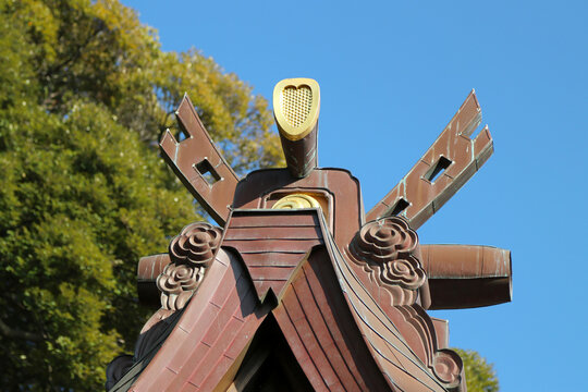 Roof end design image of the Japanese Kamakura period wooden shrine architecture. With trees an sunny sky background.