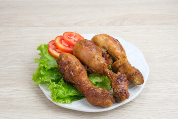 Grilled Chicken or Ayam Bakar with herbs and spices. Served on a plate with lettuce and tomatoes.
