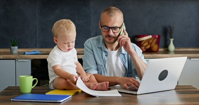 Businessman discusses issue with colleague and takes care of son sitting on table. Father freelancer communicates with co-worker on phone about project