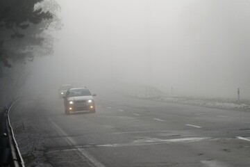 Fototapeta na wymiar Cars in the fog. Bad winter weather and dangerous automobile traffic on the road. Light vehicles in fog.