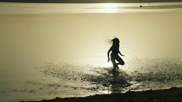 Silhouette of a happy teenage girl in a swimsuit, running jumping into the pond at sunset. Warm summer evening on vacation. Outdoor activities in the countryside