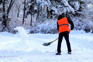 Clearing street from snow. A worker, janitor in yellow vest, cleans city street, park from snow...