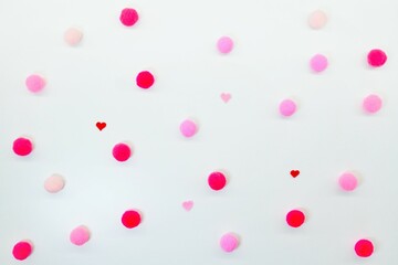 白い柔らかい布を背景に赤やピンクのポンポンと小さなハートを散りばめた水玉模様