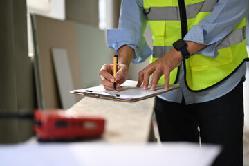 Engineer in reflective vest standing in construction site and checking building construction progress