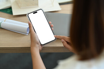 Over shoulder view of female office worker using smart phone while sitting at her working desk