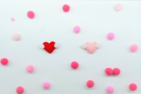 白地に毛玉で作った水玉模様の背景にバレンタインをイメージした赤とピンク色の羽つきハートの背景