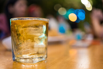 Selective focus a glass of drink alcohol mixed with water and soda in glass with ice cube on wood table at night pub.