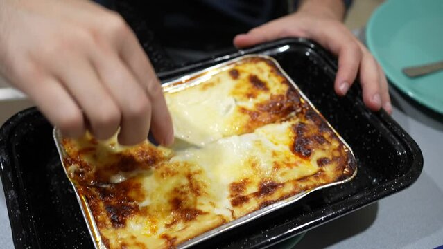 Cutting slices of a hot lasagne on a tray