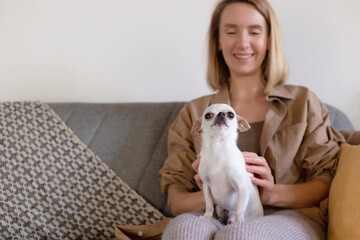 Woman strokes small dog sitting on couch.