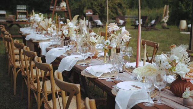 Close-up table served and decorated with candles and dried and pastel flowers for boho style wedding dinner, plates and wine glasses, no people shot, slow motion.