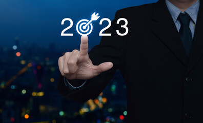 Businessman pressing 2023 letter with goal icon over blur colorful night light modern city tower and skyscraper, Business happy new year 2023 success concept