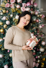 portrait of beautiful brunette smiling asian woman with a gift near christmas tree