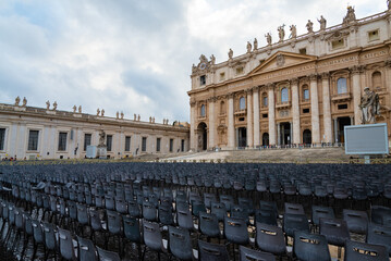 Naklejka premium Empty seats in front of the facade of the famous Saint Peter Basilica, in Vatican city, Rome, Italy. Overcasted sky on the background.