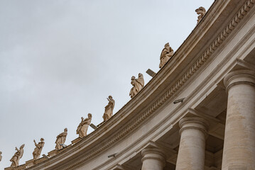 Ancient colonnade with marble statues representing saints in the famous Saint Peter square, in Vatican city, Rome, Italy. Gray sky on the background.