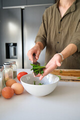 Unrecognizable asian young man putting chopped chinese chive in a bowl at kitchen.