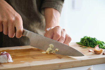 Close up of asian young man hands cutting garlic at kitchen.
