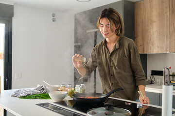 Asian young man adding spices to prepare chinese or taiwanese tomato scrambled eggs at kitchen.