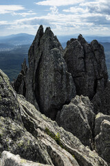 Formidable sharp gapped grey rocks on peak of mountain and panorama view on valley with slopes of mountains in silhouette, bright clouds, sunbeams in sunny summer day, view point, vertical, closeup.