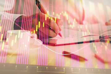 Double exposure of man's hands writing notes of stock market with forex chart.