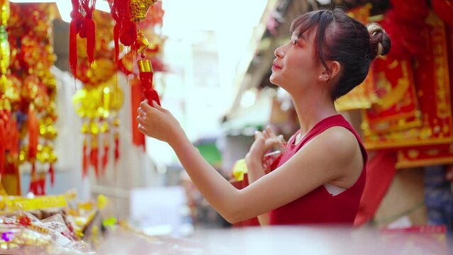 Attractive Asian woman choosing and buying decorative ornaments and joss paper for celebrating Chinese Lunar New Year festival at Bangkok Chinatown street market. Chinese culture celebration concept.