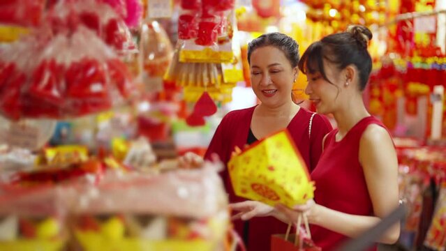 Happy Asian woman mother and daughter holding shopping bag during buy home decoration and joss paper for celebrating Chinese Lunar New Year festival at Chinatown street market. Chinese culture concept