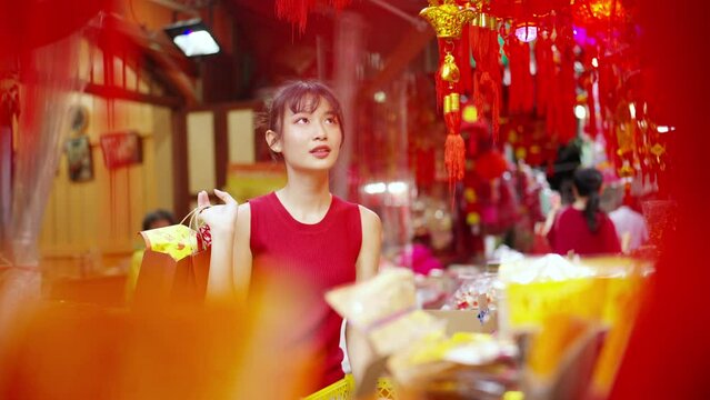 Attractive Asian woman choosing and buying decorative ornaments and joss paper for celebrating Chinese Lunar New Year festival at Bangkok Chinatown street market. Chinese culture celebration concept.