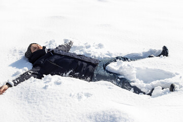 Fototapeta na wymiar A man fell in a snowdrift with his arms outstretched to his sides. Winter fun outside on a sunny day
