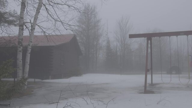 Foggy house with swing set and trees in back yard during winter.